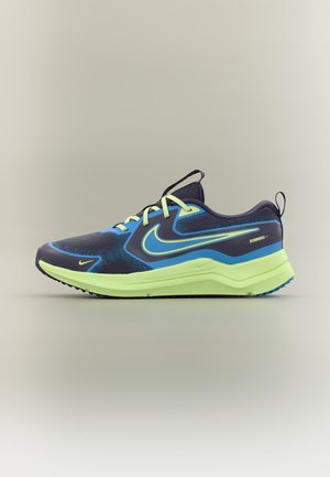 Chaussure de course Nike pour hommes en bleu marine avec une semelle et des accents vert clair, présentant un grand logo Swoosh et une fermeture à lacets.