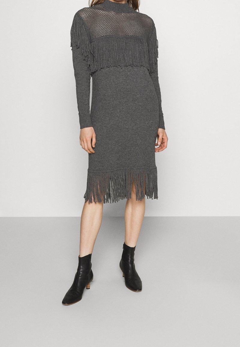 Robe tricotée grise avec un haut court à franges, des manches longues et une jupe mi-longue. Présente un design texturé en tricot ouvert sur la partie supérieure.