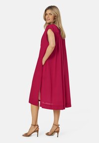 Kortärmad, löst sittande klänning i klar fuchsia, med sidofickor och ett flödande mönster. Bärs med bruna remsandaler.