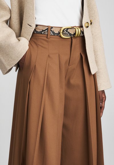 Beige knit jacket worn over white top, paired with high-waisted brown pleated skirt and snakeskin belt with gold buckle.