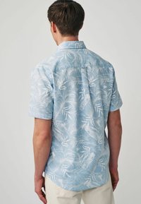Cămașă cu mânecă scurtă, de culoare albastru deschis, cu un sistem de închidere cu nasturi, având un model cu frunze tropicale albe și detalii pe spate. Fabricată dintr-un material respirabil.