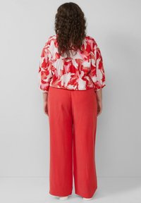 Rode bloemenblouse met korte mouwen, gecombineerd met brede koraalkleurige broek. De stof lijkt glad en de blouse heeft een vloeiende uitstraling.