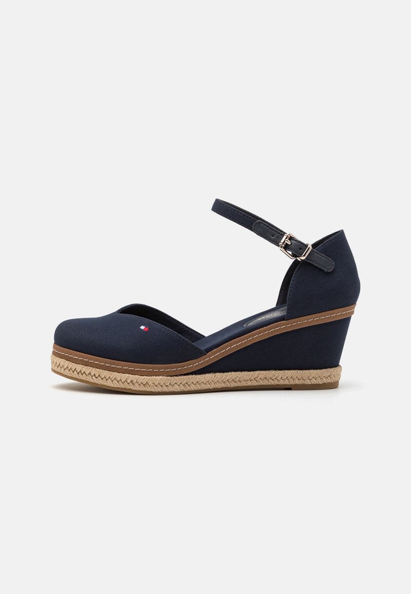 Laivastonsininen korkkipohjallinen kengät nilkkahihnalla, solkikiinnitys, ruskealla reunuksella, kudottu espadrillo-tyylinen pohja ja pieni punaiset ja valkoiset logo etuosa.
