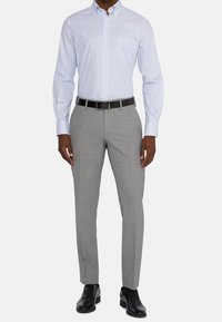 Jasnoniebieska i biała koszula w paski na guziki z pojedynczą kieszenią na piersi, zestawiona z jasnoszarymi, dopasowanymi spodniami i czarnymi skórzanymi butami.