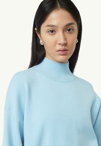 Helles, blaues Rollkragensweatshirt mit Rippkragen und überschnittenen Schultern, aus weichem Strickmaterial gefertigt. Hat eine lockere Passform.