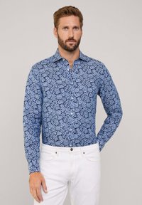 Camisa de manga larga en azul con un patrón de hojas, hecha de tela ligera. Presenta un cuello abotonado y un corte recto. Se combina con pantalones blancos.