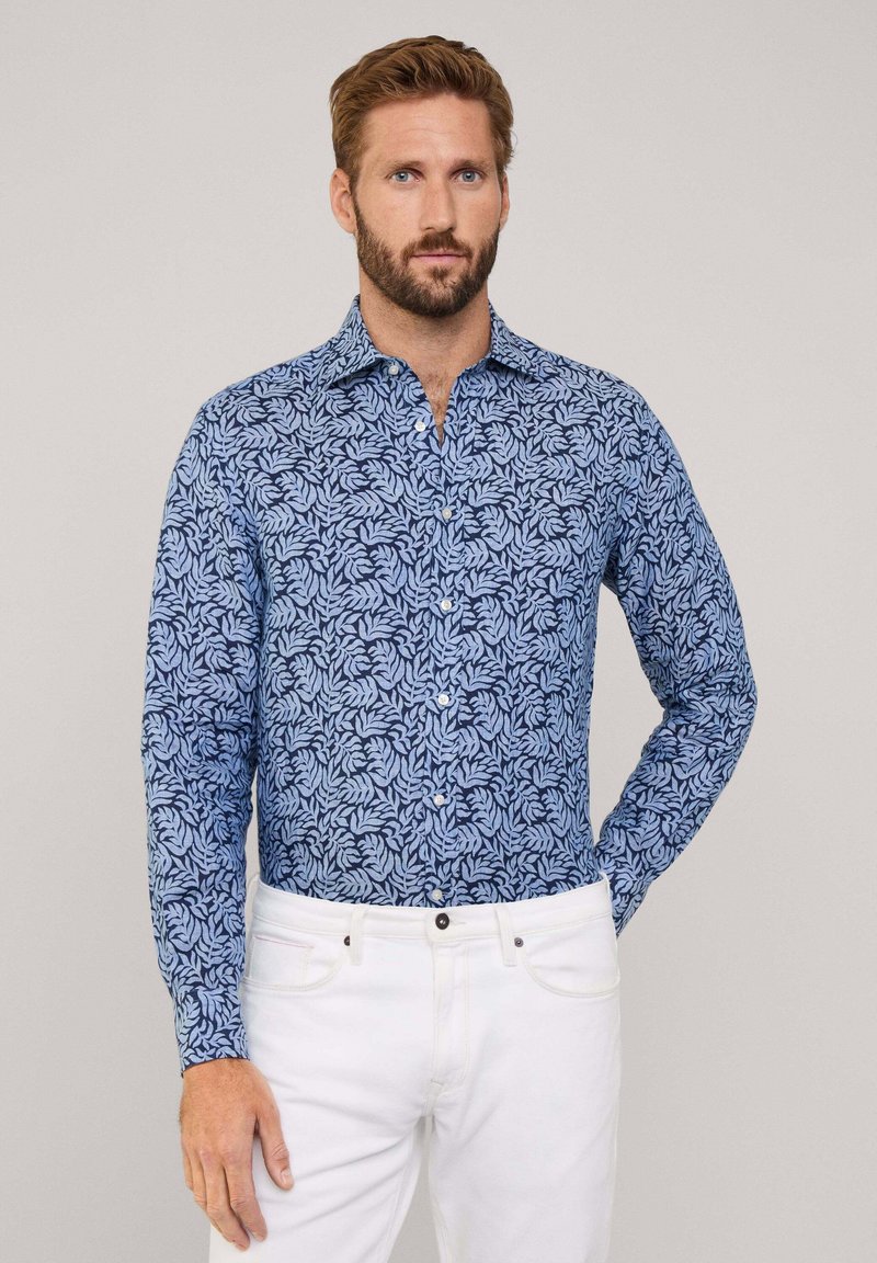 Camisa de manga larga en azul con un patrón de hojas, hecha de tela ligera. Presenta un cuello abotonado y un corte recto. Se combina con pantalones blancos.