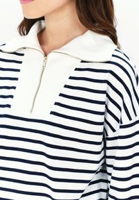 Pullover bianco e blu a righe con colletto con zip, caratterizzato da un tessuto morbido e testurizzato e una vestibilità comoda.