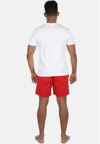 Hvid kortærmet t-shirt og r�øde badeshorts, set fra ryggen. Shortsene er lavet af et letvægtsmateriale og har en elastisk talje.