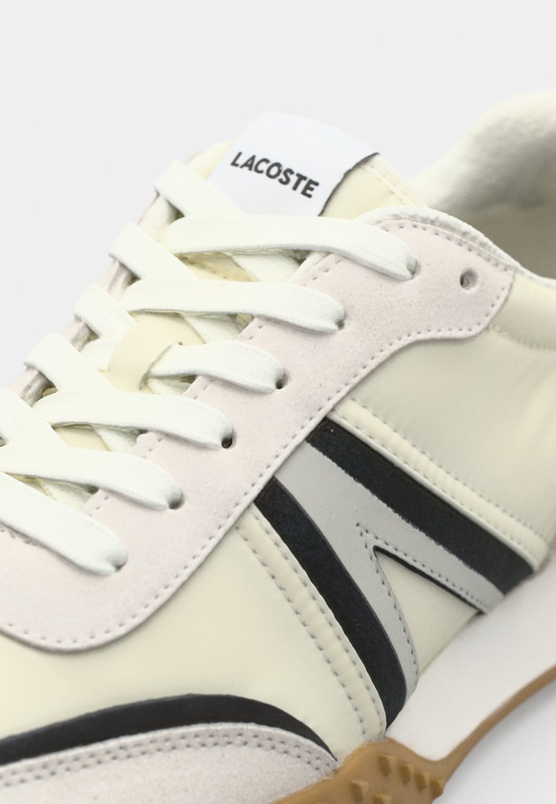 Baskets blanches et crème avec des accents noirs et gris, dotées d'un cuir lisse et de daim. Comprend des lacets plats et une semelle en caoutchouc.