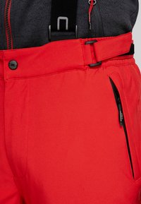 Röda skidbyxor har en elegant design med justerbara remmar, ett ficklock med dragkedja och texturerat tyg för ökad komfort och prestanda.