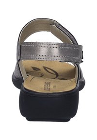 Černé sandály s metalickým stříbrným páskem kolem kotníku, plochou podrážkou a měkkou stélkou. Mají prošívané detaily a otevřený design paty.