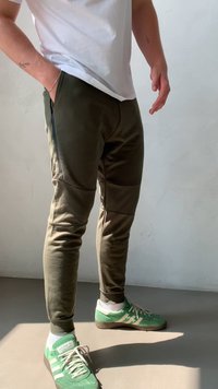 Joggers de color verde oscuro, hechos de una tela suave y con un corte ceñido, que presentan bolsillos laterales con cremallera y paneles texturizados. Combinados con zapatillas verdes.