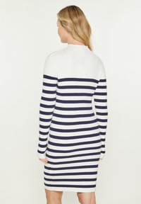 Ribbed dress with horizontal navy and white stripes, a high neck, and long sleeves. The body-hugging design accentuates the silhouette.