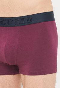 Burgundske bokserice iz mehkega blaga, z temno modrim elastičnim pasom z embosiranim logotipom. Tesno prilegajoča zasnova z minimalnimi šivi.