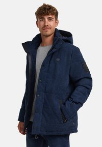 Marineblaue gepolsterte Jacke mit strukturierter Oberfläche, Kapuze, mehreren Knöpfen und einem Logopatch am Ärmel. Verfügt über seitliche Taschen und ein weiches Futter.