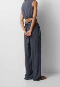 Grijze mouwloze top met een strik op de rug, gecombineerd met losse grijze pants. Zachte stof met een gladde textuur, ontspannen pasvorm en subtiele drape.