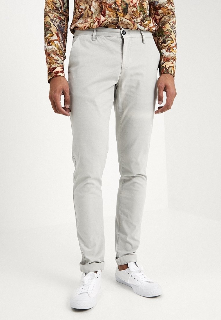 Pantalon gris clair slim-fit avec poignets, porté par une personne, assorti à des baskets blanches et un haut à manches longues coloré avec un imprimé animal.