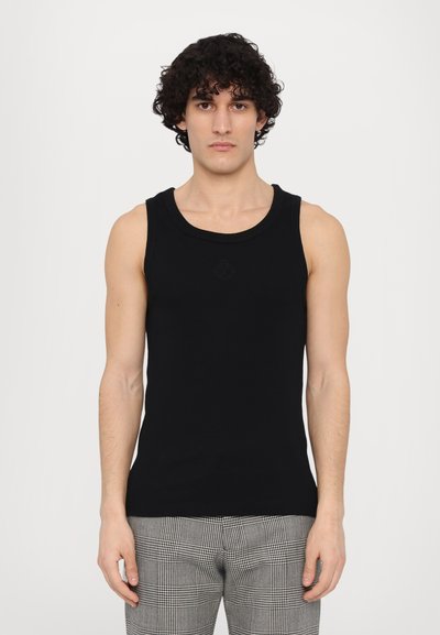 Zwarte katoenen tanktop met een ronde halslijn en ribbeltextuur. Model draagt het met gewatteerde grijze broeken, wat een getailleerd ontwerp laat zien.