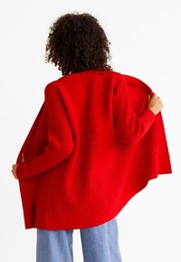 Rode geribbelde cardigan met lange mouwen, open voorkant en losse pasvorm. Heeft een gestructureerd oppervlak; de achterkant toont een vloeiende stof en drape.