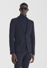 Mornarska sako jakna s jednim gumbom, vrhunskim reverima i bočnim džepovima, nosi se preko teksturiranog mornarskog pletiva s rolkragnom. Slim fit dizajn.