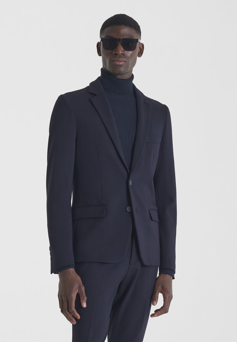 Mornarska sako jakna s jednim gumbom, vrhunskim reverima i bočnim džepovima, nosi se preko teksturiranog mornarskog pletiva s rolkragnom. Slim fit dizajn.