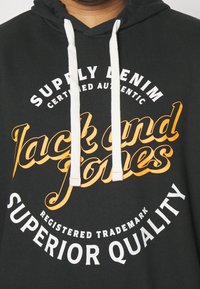 Svart huvtröja med vit och orange textdetalj, försett med snörning och en mjuk tygtextur.