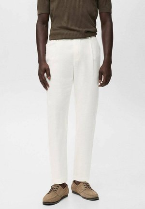 Pantalones de lino blancos con corte recto, con bolsillos laterales. Combinados con zapatos beige de cordones y una camiseta corta de manga corta en color oliva con canalé.