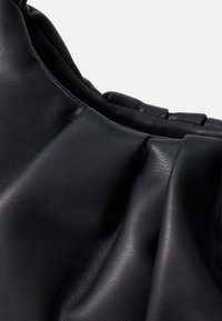 Gros plan sur un cuir noir souple avec des détails froncés et une texture subtile sur un fond blanc uni.