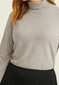 Szary sweter z golfem wykonany z miękkiego dzianiny o dopasowanym kroju. Kołnierz jest ściągaczowy, zestawiony z prostą czarną spódnicą w talii.