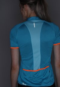 Camisa deportiva azul con textura de malla, acentos naranjas en contraste, detalles reflectantes y un diseño ajustado. Cuenta con un bolsillo trasero para almacenamiento.