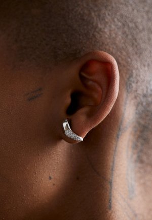 Silver earring with a curved design featuring a section of sparkling stones, attached to the ear of a person with short hair.