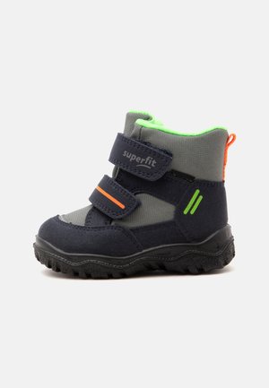 Botte d’hiver enfant bleu foncé et gris avec doublure vert néon, deux bandes Velcro, accents orange et semelle noire robuste.