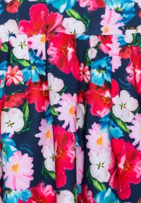 Kukkakuvioinen mekko tummansinisellä taustalla. Ominaisuuksiin kuuluvat suuret vaaleanpunaiset, punaiset ja siniset kukat, poimutettu muotoilu sekä koristeellinen "Guess"-logo.