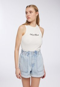 Canottiera bianca a coste con testo "Venice Beach"; abbinata a pantaloni shorts in denim chiaro con orli arrotolati e vita alta.