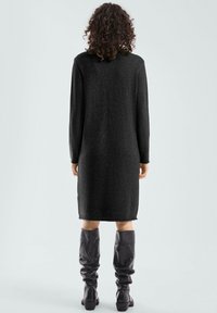 Robe en tricot noire à manches longues, longueur mi-mollet et coupe décontractée. Associée à des bottes en cuir noires, hautes et ajustées.