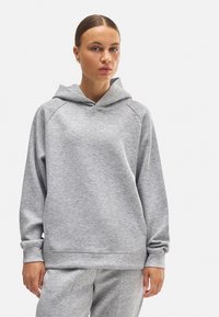 Sudadera con capucha gris de tejido suave, con un corte relajado, mangas raglán y un bolsillo canguro en la parte delantera. Textura suave y diseño minimalista.