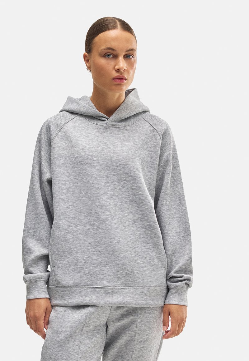 Sudadera con capucha gris de tejido suave, con un corte relajado, mangas raglán y un bolsillo canguro en la parte delantera. Textura suave y diseño minimalista.