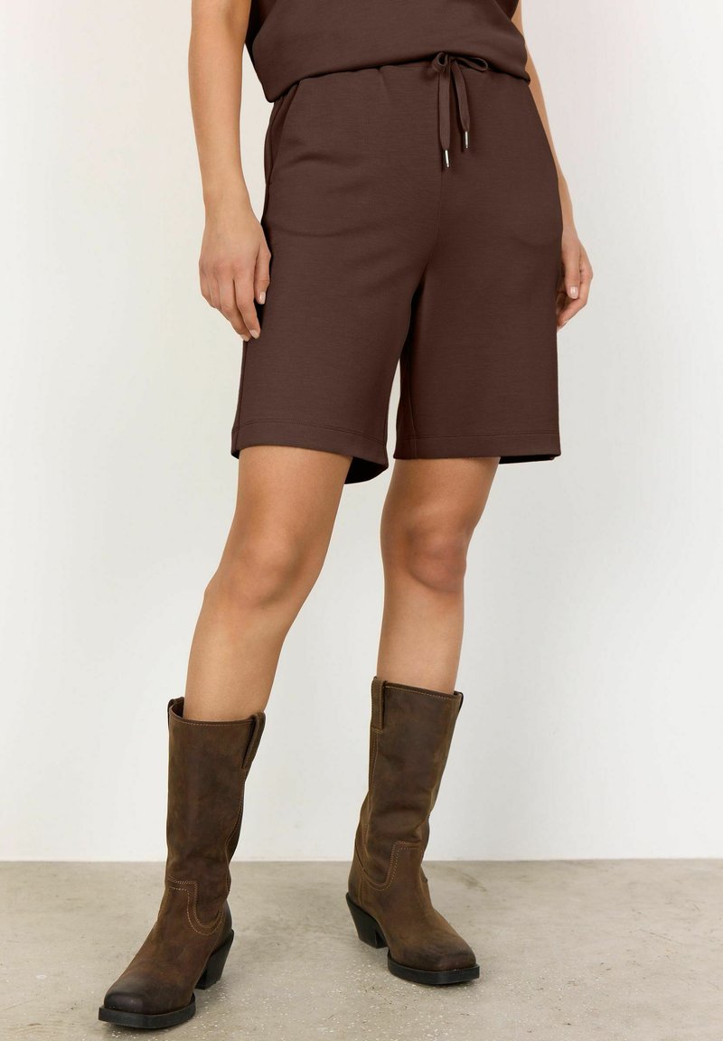 Pantaloni corti in cotone marrone con vita elastica e cordoncino, dotati di tasche laterali e una vestibilità morbida, abbinati a stivali alti in pelle marrone.
