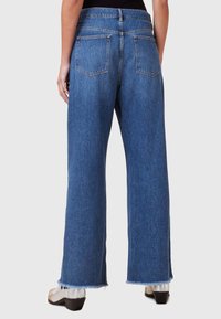 Jeans de mezclilla de pierna ancha en un lavado azul medio. Presentan una cintura alta, dos bolsillos traseros y dobladillo deshilachado. Tejido texturizado con costuras visibles.