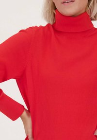Rode coltrui gemaakt van een zachte brei materiaal. Bevat lange mouwen met een geribde manchette en een naadloos ontwerp op de schouders.