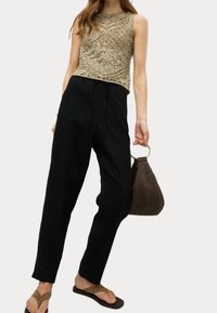 Pletené zlaté tílko s geometrickým vzorem, černé kalhoty na stažení, hnědá semišová kabelka s kruhovým uchem a hnědé žabky.