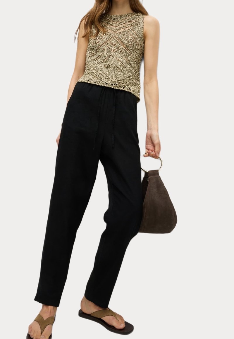 Pletené zlaté tílko s geometrickým vzorem, černé kalhoty na stažení, hnědá semišová kabelka s kruhovým uchem a hnědé žabky.