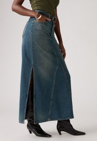 Denim maxiskjørt med høy splitt, blåfarge, med kontrasterende sømmer og en tettsittende midje. Kombinert med knæhøye svarte støvler.