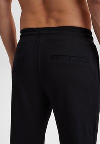  Sorte, tætsiddende bukser med en glat tekstur, der har en flad baglomme og en elastisk talje for komfort og nem påklædning.