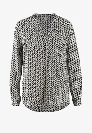 Blouse à motifs noir et blanc avec un col en V et des manches 3/4, associée à un pantalon slim noir et des chaussures noir et blanc.