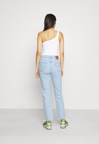 Jeans de denim azul claro con un corte recto, terminaciones recortadas y un acabado desgastado. Combinados con una blusa blanca de un solo hombro y zapatillas coloridas.