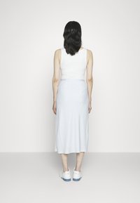 Svetle modrá midi sukně s hladkou texturou, spárovaná s bílým topem bez rukávů. Bílé tenisky viditelné dole, zdůrazňující ležérní styl.