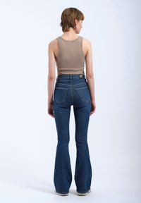 Flared blue denim jeans with a high waist and two back pockets, paired with a beige ribbed tank top. The model is shown from behind.