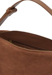 Brun mockaklädhandväska med zippered topp, utrustad med ett slätt läderhandtag och en inre dragkedjeficka. Strukturerad utsida och tygfoder.